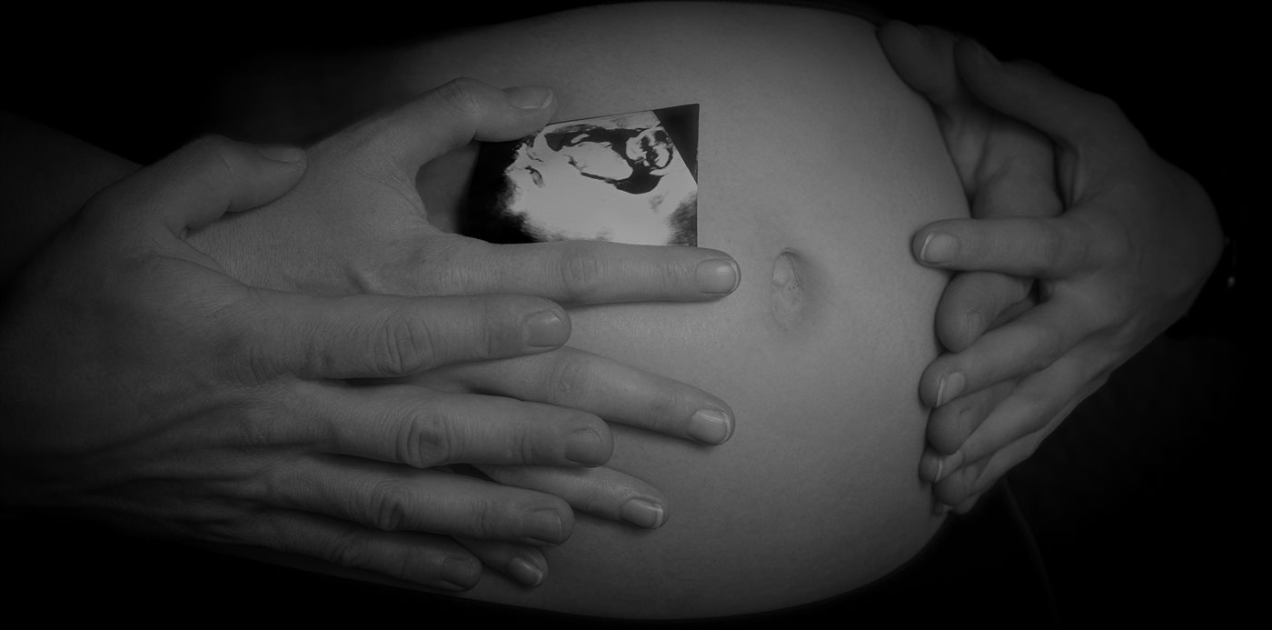 Babybauch mit Ultraschallbild, die Hände beider Eltern liegen darauf, schwarzweiß