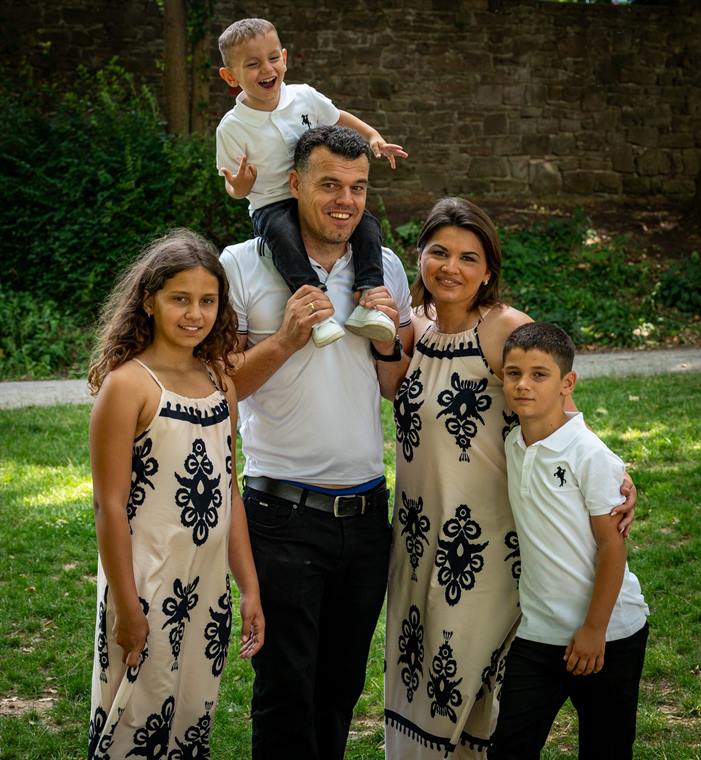 Familie mit drei Kindern im Garten, der Vater trägt den Jüngsten auf den Schultern